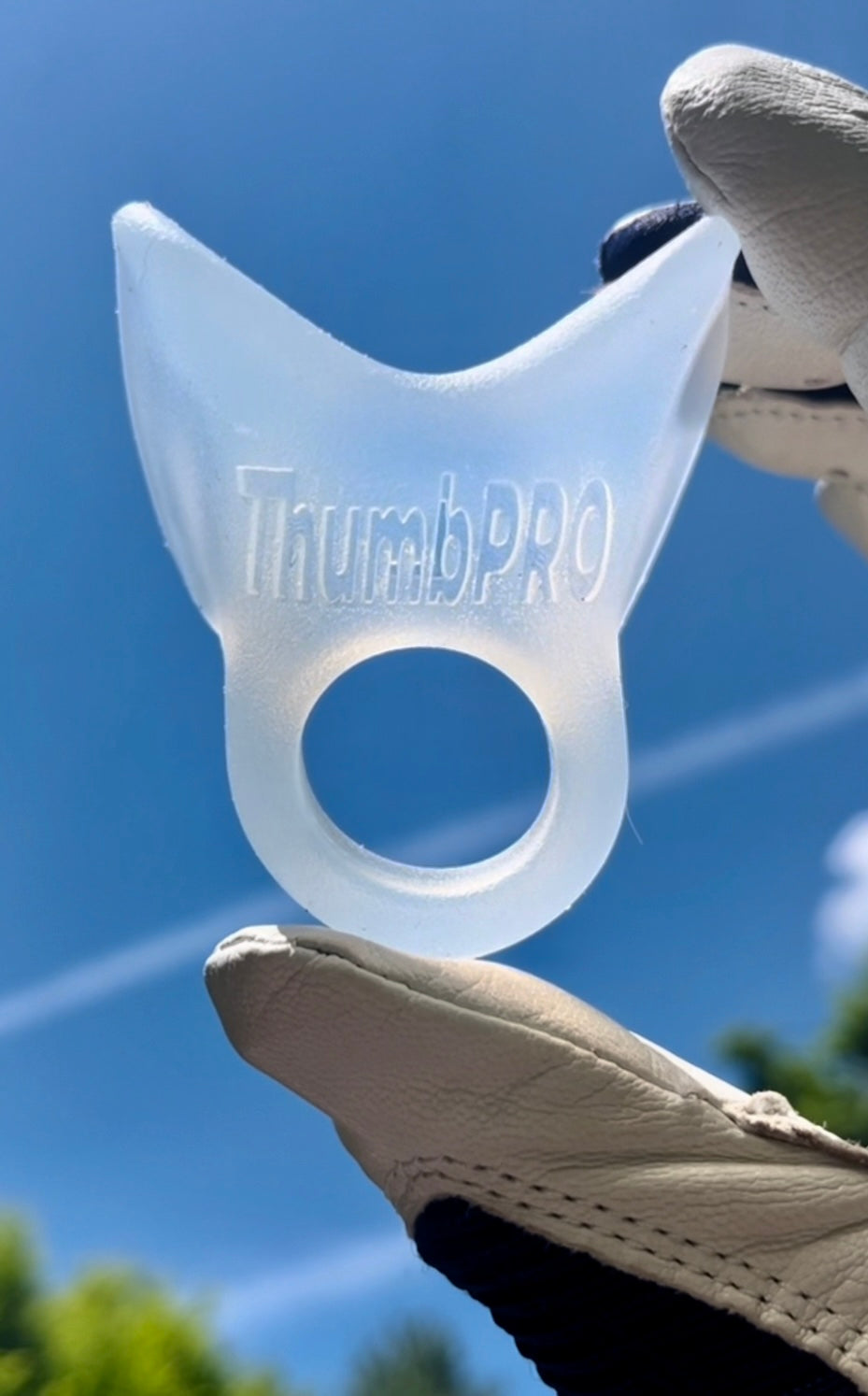 Clear 'ThumbPRO' baseball thumb guard protector held by a gloved hand against a blue sky.